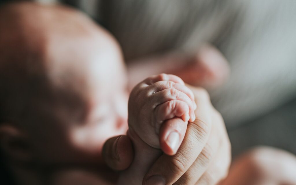 Adult hand holding a newborn baby hand
