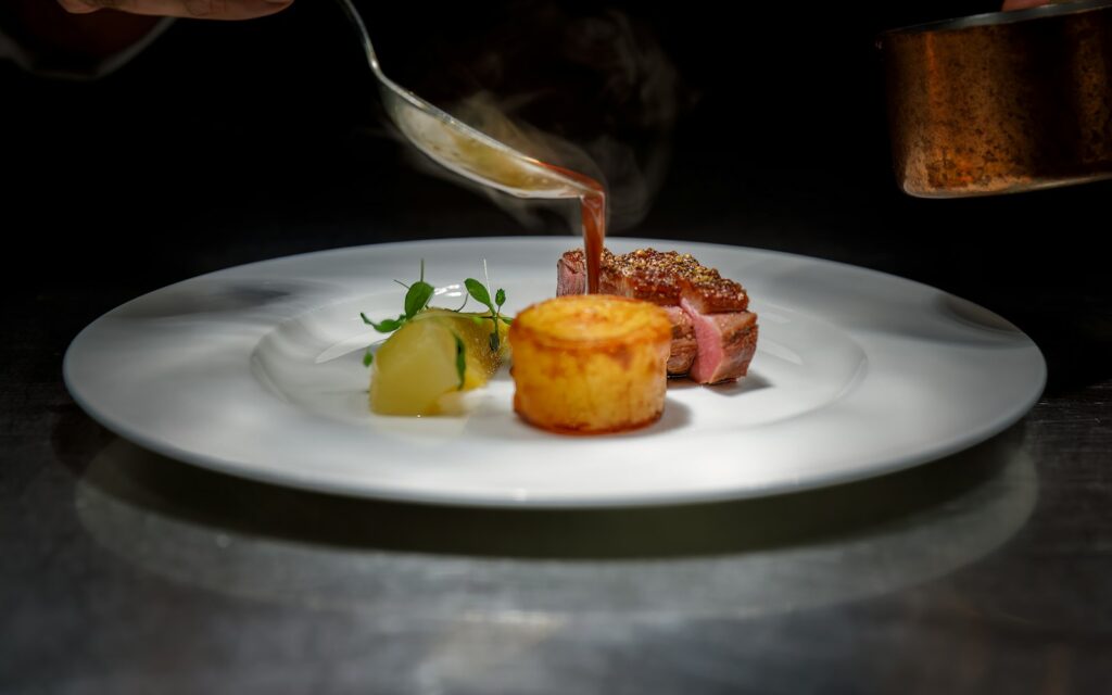 Private chef pouring sauce over a plated dish