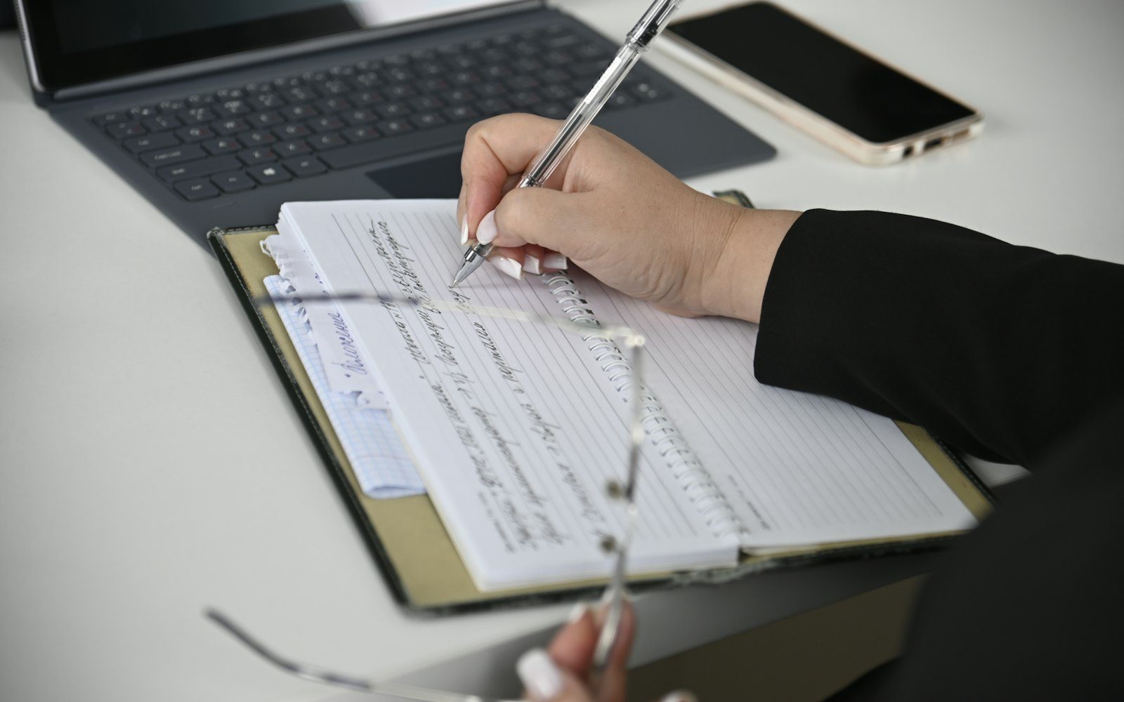 Writing a resume in a notebook next to a laptop